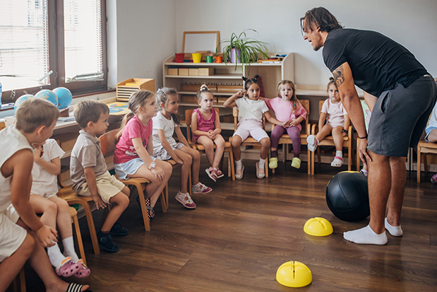 Animateur périscolaire encadrant un groupe d'enfants lors d'une activité collective en école maternelle, illustration d'un article consacré à la professionnalisation et à la réforme du métier d'animateur vacataire.